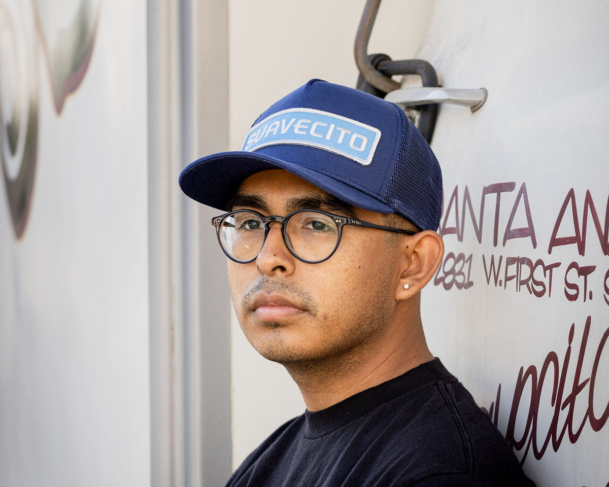 man wearing - blue suavecito hat with white embroidered text and light blue background "suavecito"