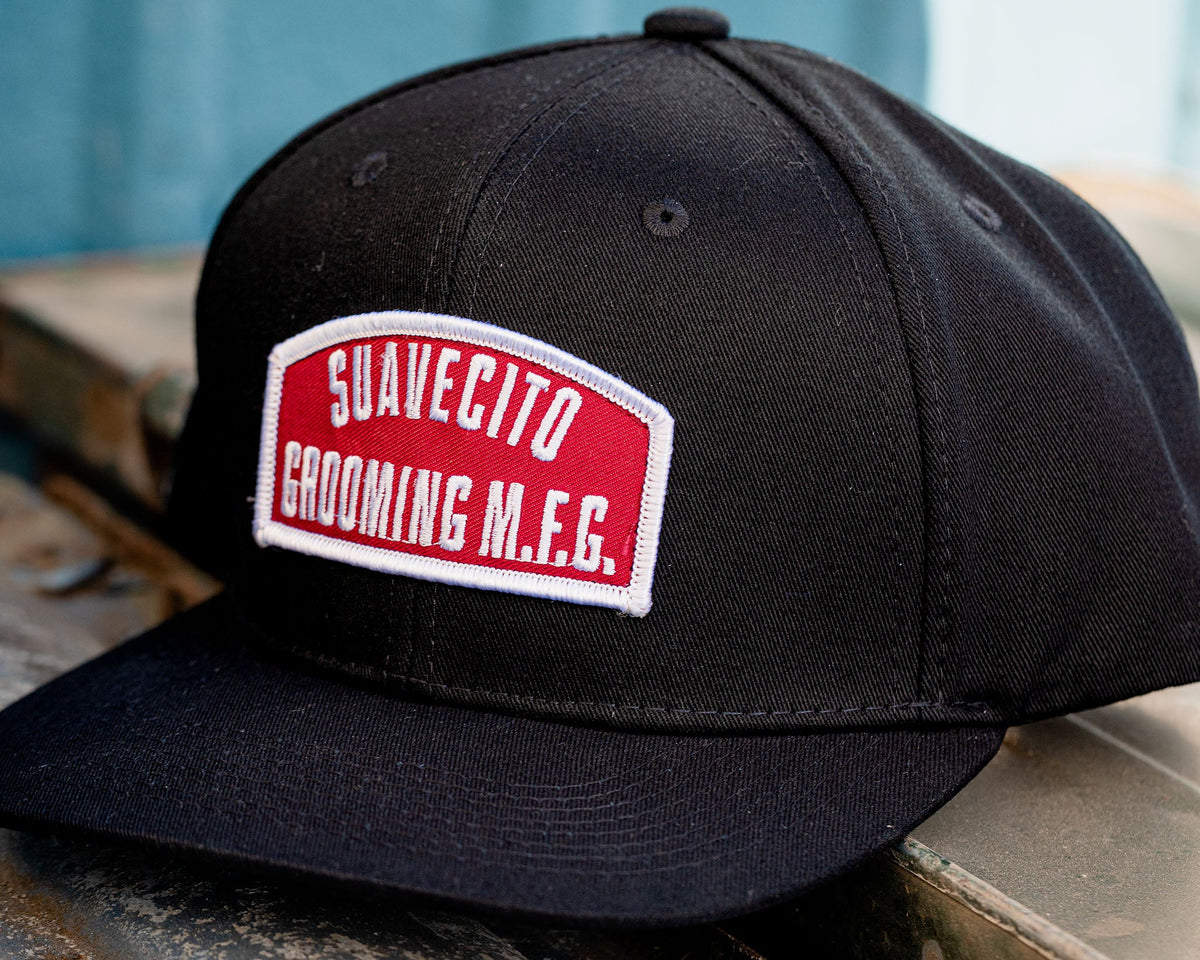 suavecito hat with embroidered text and red background "suavecito grooming m.f.g."