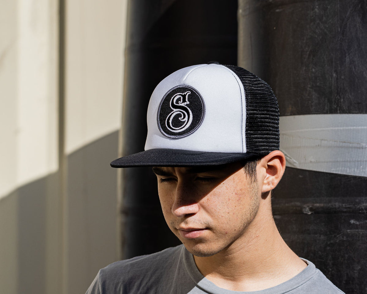 man wearing - suavecito hat with white embroidered text and black background with suavecito "S"