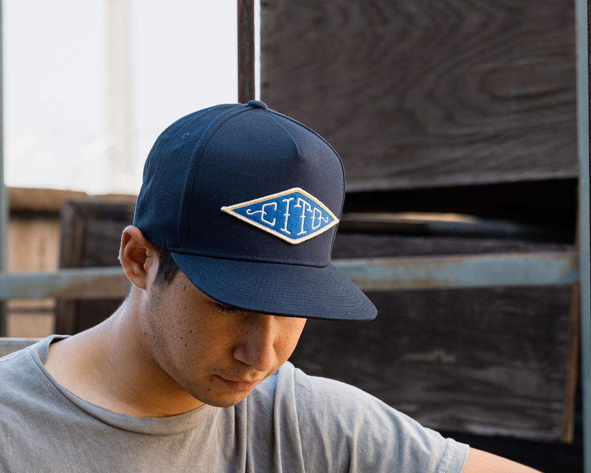 man wearing - blue suavecito hat with white embroidered text and blue background "cito" in diamond shape