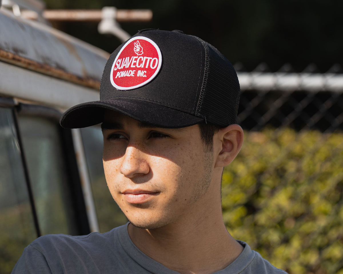 man wearing - black suavecito hat with white embroidered text and red background "suavecito pomade inc."
